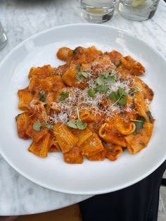 a white plate topped with pasta covered in sauce and parmesan cheese