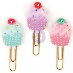 three different colored cupcakes with bows on them are sitting on paper clip holders