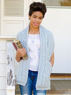 the woman is wearing a blue cardigan and holding a book in her hands while standing next to a white door