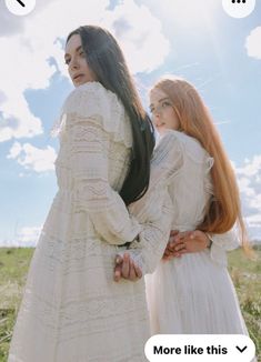 two women standing next to each other in front of a sky with clouds and grass