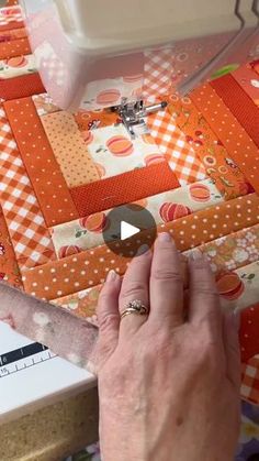 a person is using a sewing machine to sew on an orange and white quilt