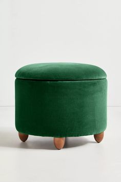 a green ottoman with wooden legs and an upholstered foot rest on a white floor