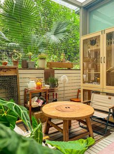 a wooden table sitting on top of a patio next to a plant filled with potted plants