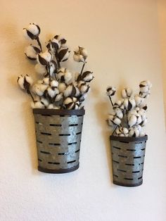 two metal buckets holding cotton plants against a white wall, one is made out of tin cans