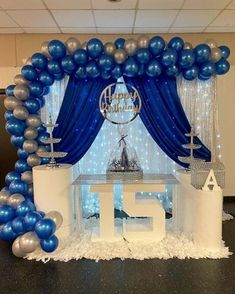 a table with blue and silver balloons in front of a stage set up for a birthday party