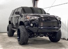 a black toyota truck parked in front of a garage door with large tires on it