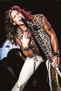 a man with long hair and leopard print shirt holding a microphone in his right hand