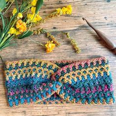 two crocheted headbands sitting on top of a wooden table next to flowers