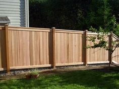 a wooden fence next to a tree in a yard with green grass and trees behind it