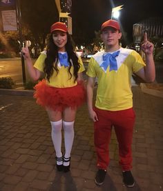 two people dressed up in costumes standing on a brick walkway at night time with one person wearing a yellow shirt and red tutu skirt