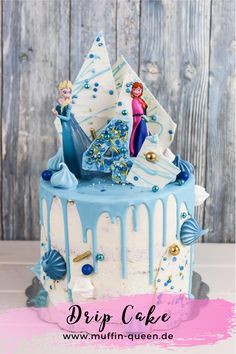 a frozen princess cake with blue icing and decorations on top, sitting in front of a wooden background