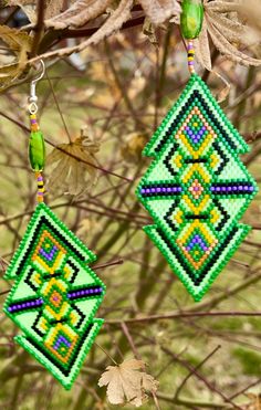 two green and yellow beaded earrings hanging from a tree branch with leaves in the background