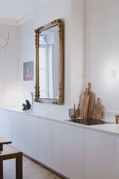 a kitchen with white cabinets and wooden cutting boards on the counter top next to a large gold framed mirror