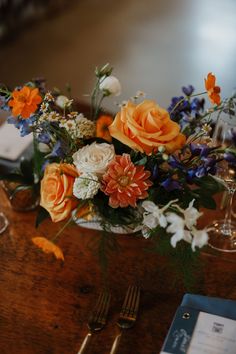 an arrangement of flowers in a vase on a table with silverware and wine glasses