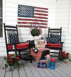 an american flag is hanging on the wall next to two rocking chairs with red, white and blue pillows