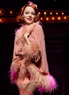 a woman standing on top of a stage wearing a pink dress and feathered coat