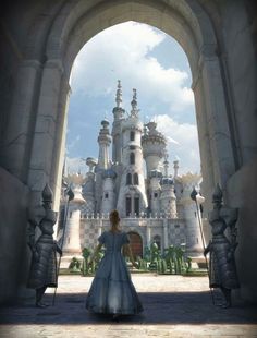 a woman in a blue dress is standing under an archway with a castle in the background