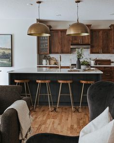 an open kitchen and living room area with bar stools in the center, wood flooring