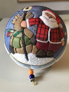 a small round box with santa clause on it's back and decorations hanging from the front