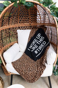 a wicker chair with a black pillow on it and some plants in the background