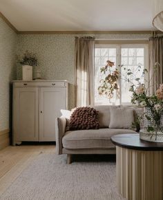 a living room filled with furniture and flowers on top of a table in front of a window