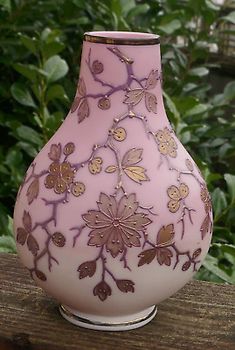 a pink vase sitting on top of a wooden table next to green leaves and bushes