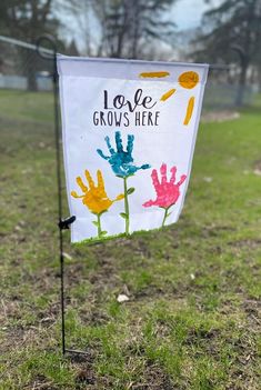 a sign that says love grows here with handprints on it in the grass