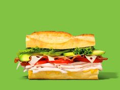 a large sandwich with meat, lettuce and tomato on a green paper background