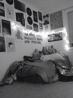 black and white photograph of a bedroom with posters on the wall, guitar propped up against the bed