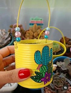 a hand holding a yellow tin can with a cactus design on it and beads around the handle