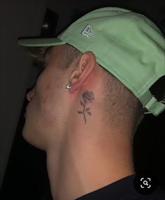 a man wearing a green hat with a rose tattoo on his left side behind his ear