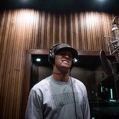 a man wearing headphones standing in front of a microphone and recording equipment on a wooden paneled wall