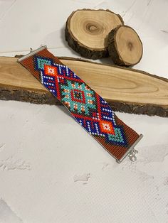 a colorful beaded bracelet sitting on top of a piece of wood next to a slice of tree