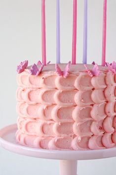 a cake with pink frosting and purple candles on it, sitting on a plate