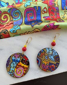 two colorful earrings sitting on top of a marble table next to a bag and scarf