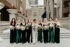 a group of women standing next to each other in front of a building holding bouquets