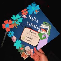 a person holding up a blue graduation cap with flowers on it and the words ha ha finally