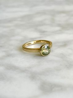 a yellow gold ring with a green stone on the front and side, sitting on a marble surface