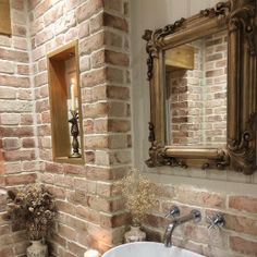 a white sink sitting under a bathroom mirror next to a brick wall in a bathroom