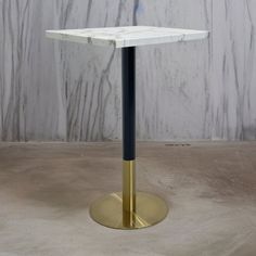 a white marble table with a black metal base and gold colored legs in front of a grey wall