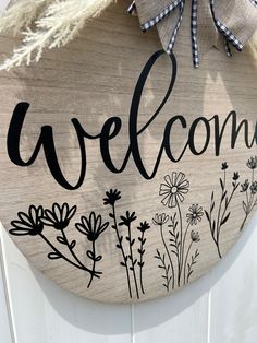 a welcome sign hanging on the side of a white door with flowers and grass painted on it