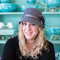 a woman wearing a hat sitting in front of shelves