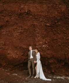 a bride and groom standing in front of a large red rock on their wedding day