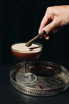 a person dipping something into a glass on a metal platter with a black background