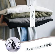 a person holding several folded clothes in one hand and the other with two tags on it