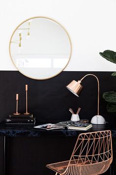 a desk with a mirror, lamp and books on it in front of a black wall