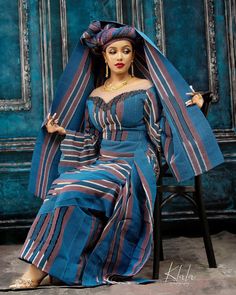 a woman sitting in a chair wearing a blue and red dress with stripes on it