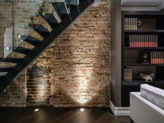 a living room filled with furniture and a stair case in front of a brick wall