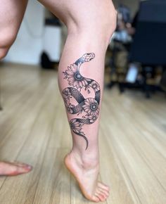 a woman's leg with a snake and flowers tattoo on it, while standing on a hard wood floor