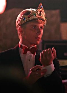 a young man wearing a crown standing in front of a microphone with his hands clasped